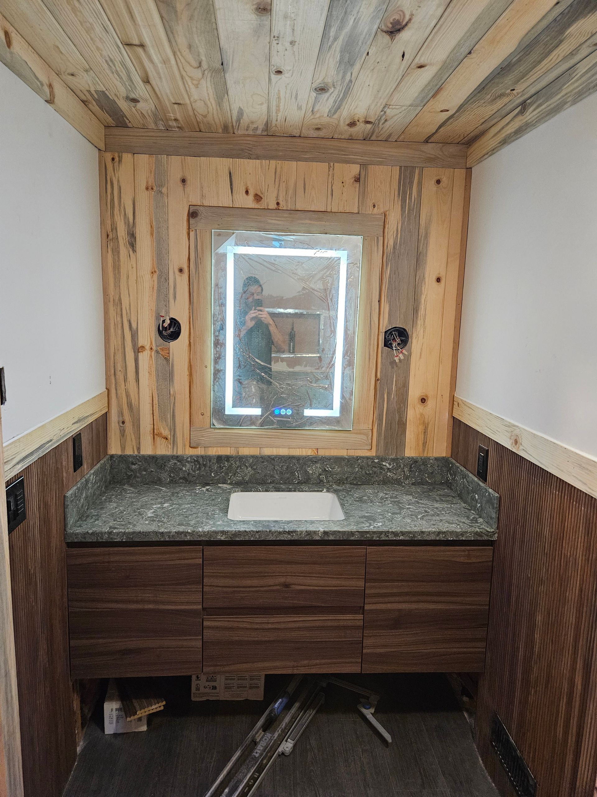 A bathroom with a sink , mirror and wooden walls.