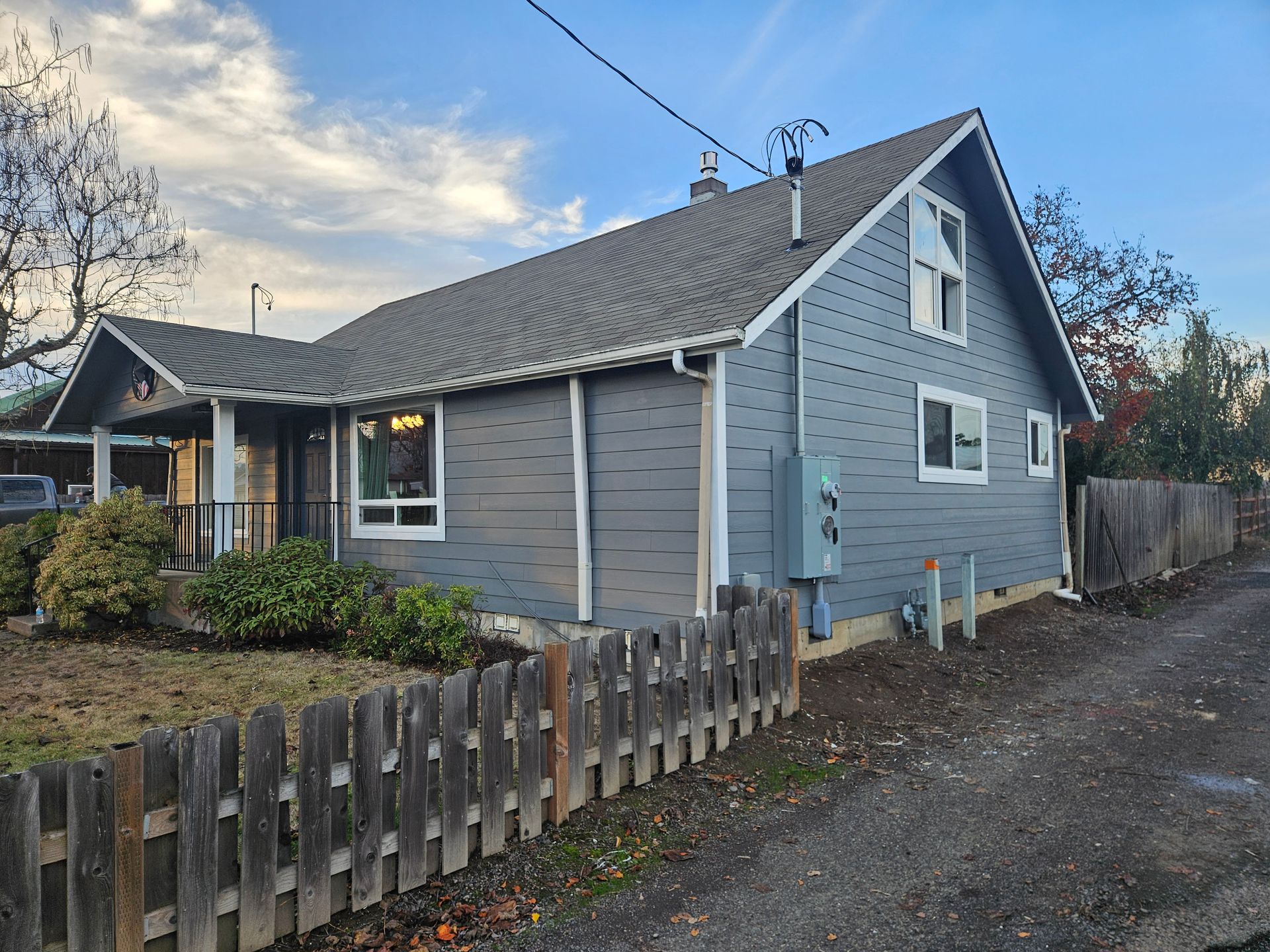 A gray house with a wooden fence in front of it.
