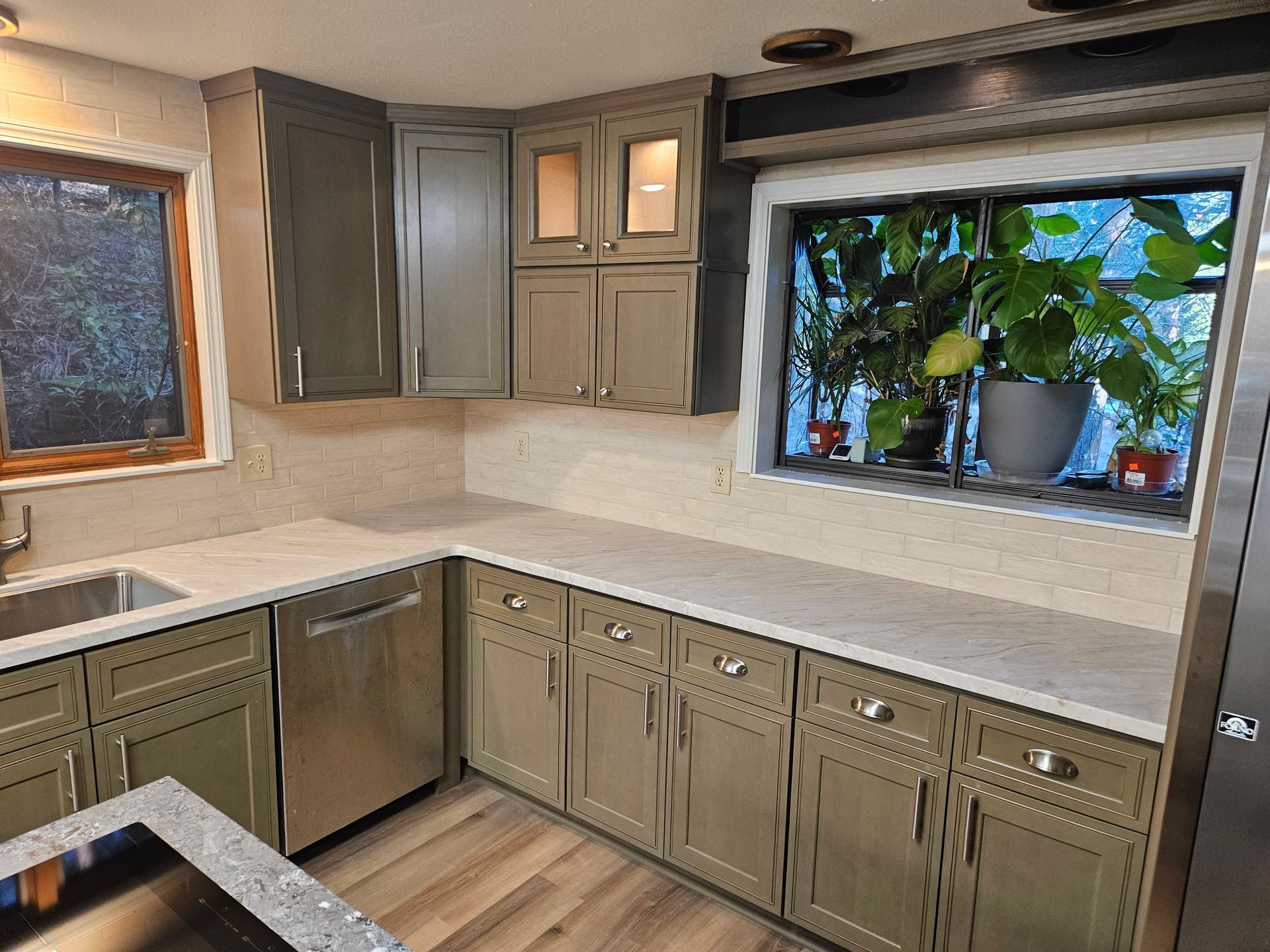 A kitchen with green cabinets , stainless steel appliances , a sink , and a window.