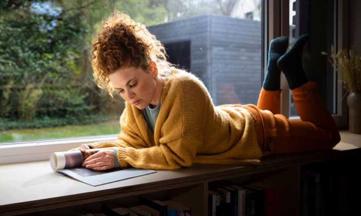 Eine Frau liegt auf einem Fensterbrett und liest ein Buch.