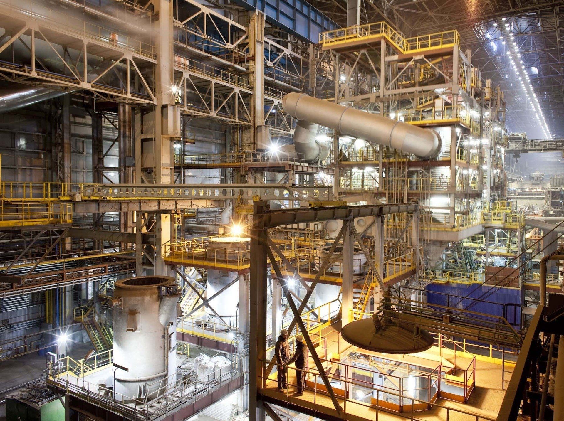 Eine große Fabrik mit vielen Rohren und Maschinen ist nachts beleuchtet.