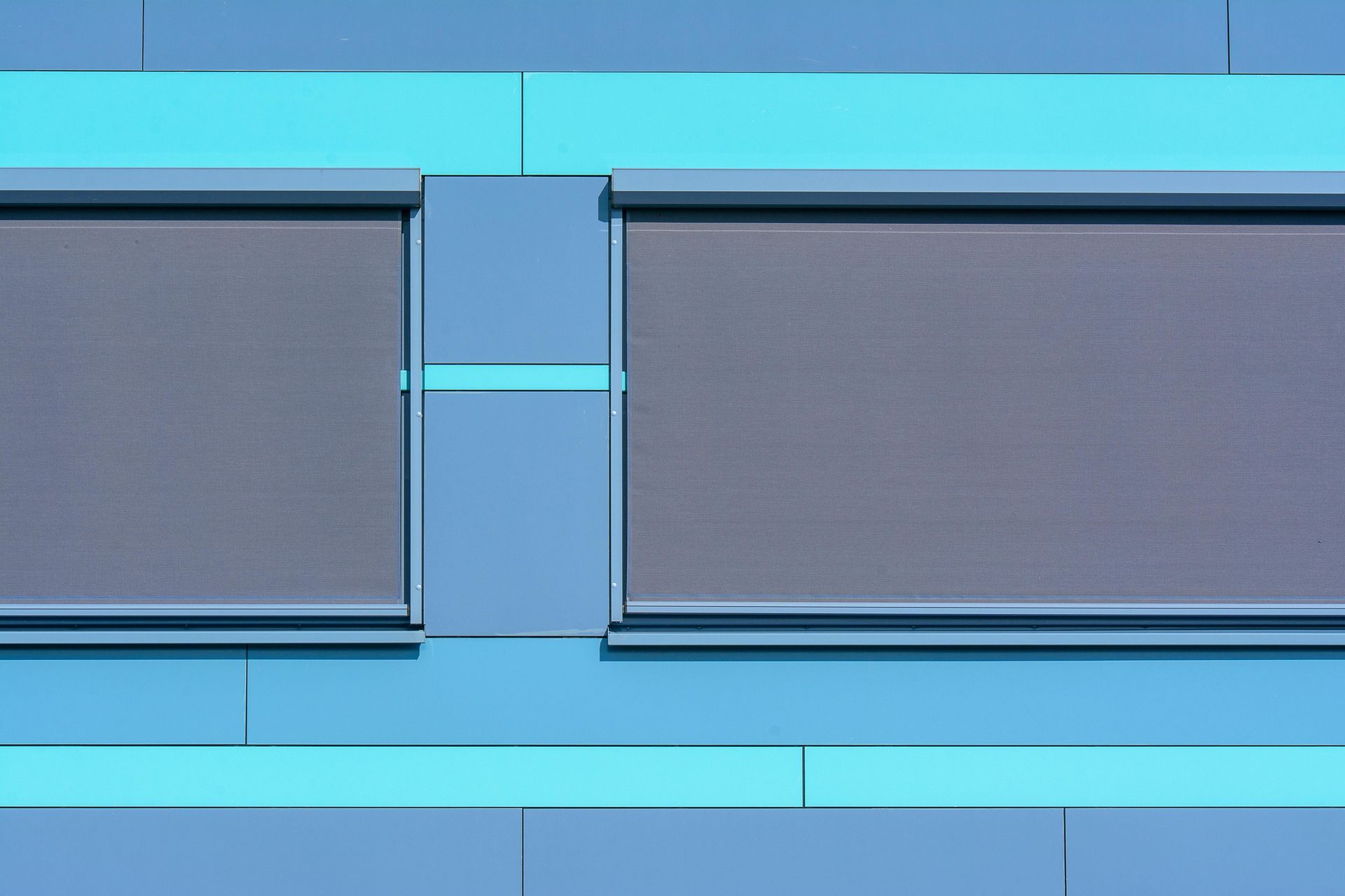 Two dark, rectangular windows are set into a blue exterior wall with horizontal turquoise and light blue trim.