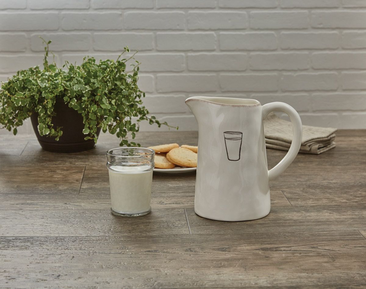 A pitcher of milk and a glass of milk are on a wooden table.