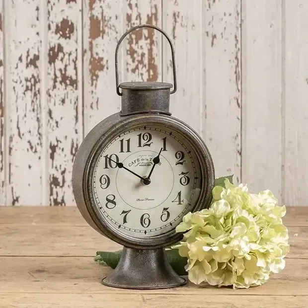A clock is sitting on a wooden table next to a flower.
