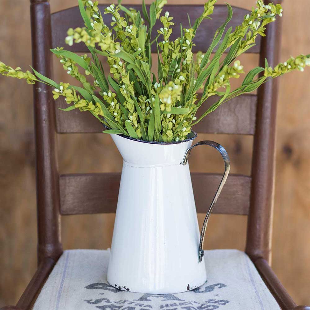 A white pitcher filled with green flowers is sitting on a chair