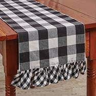 A black and white checkered table runner with ruffles is on a wooden table.