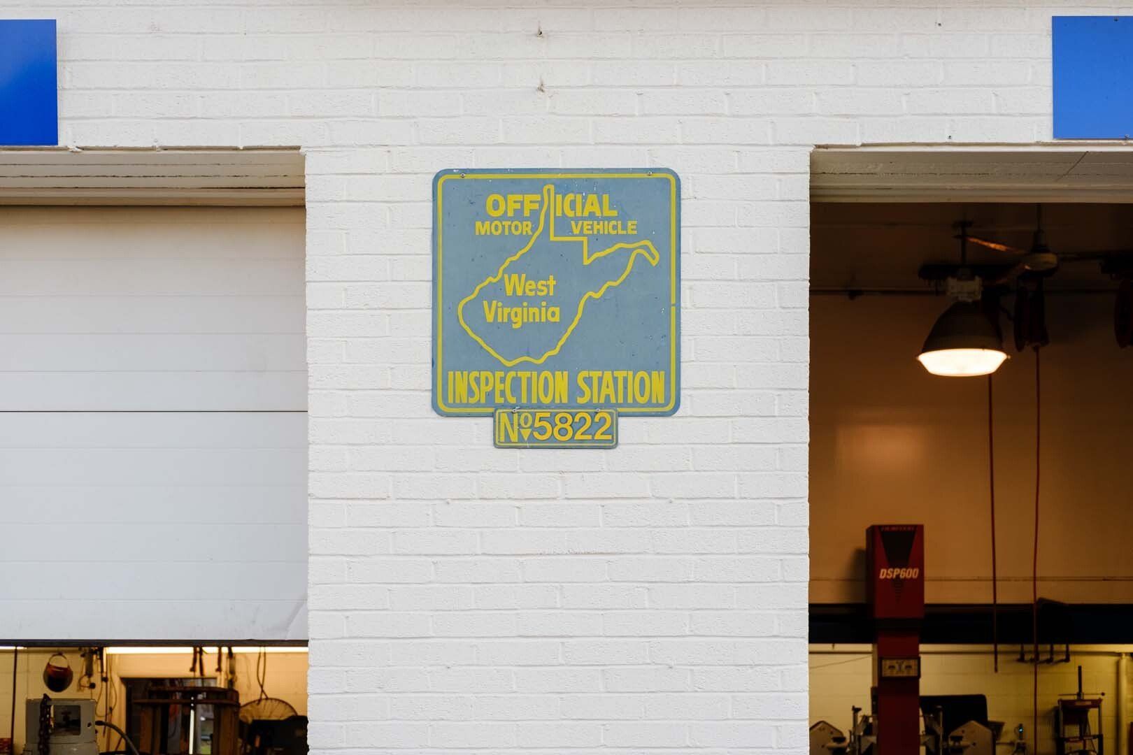 West Virginia Official Vehicle Inspection Station sign; blue and yellow, mounted on white brick wall.