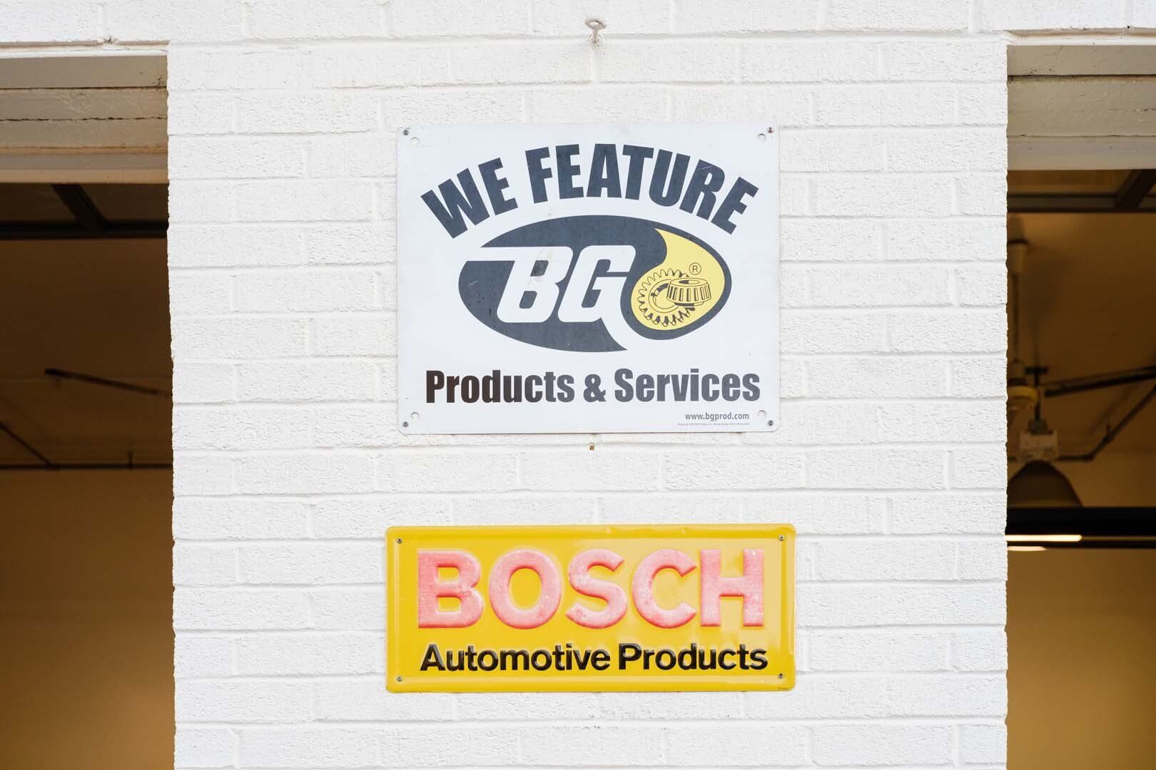 Sign for BG Products & Services, with a Bosch Automotive Products sign below, on a white brick wall.