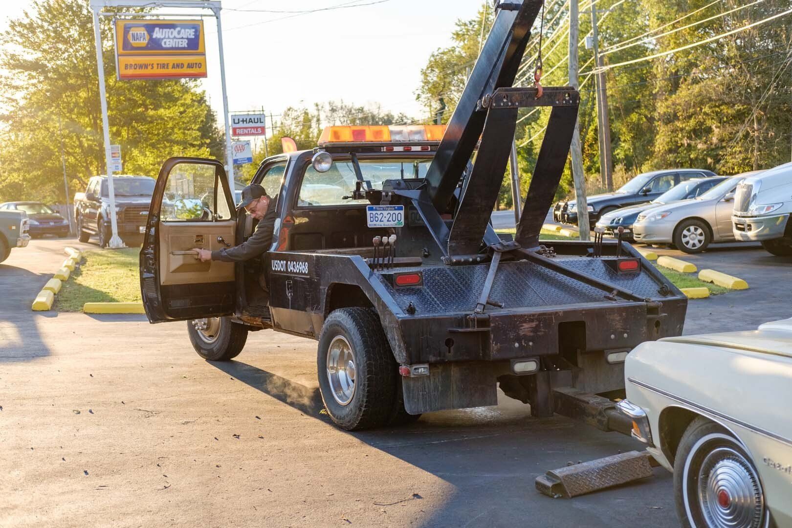 Tow truck towing a beige car at a parking lot, near an auto parts store.