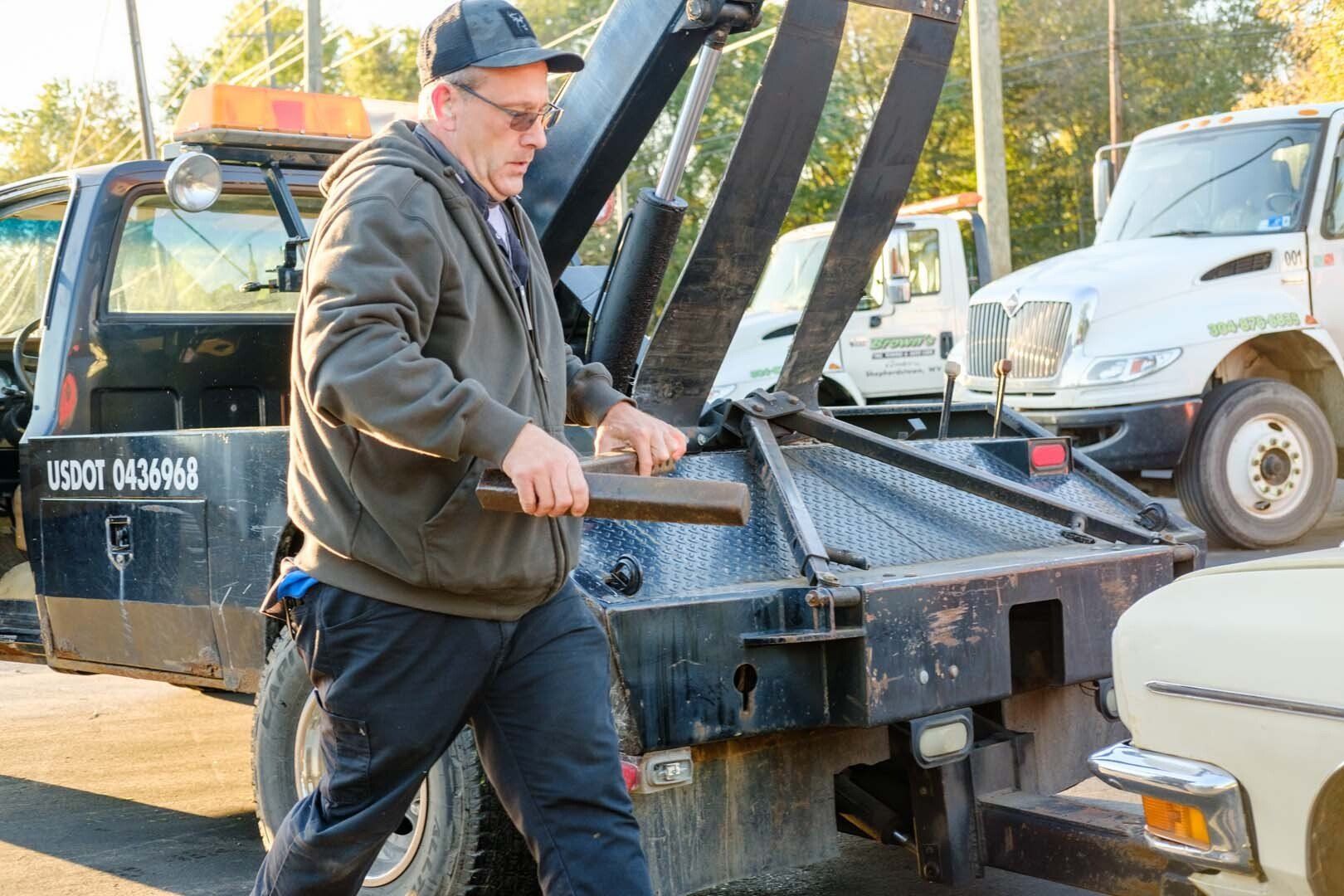 A person using a tool, possibly a tow truck driver, near a tow truck.