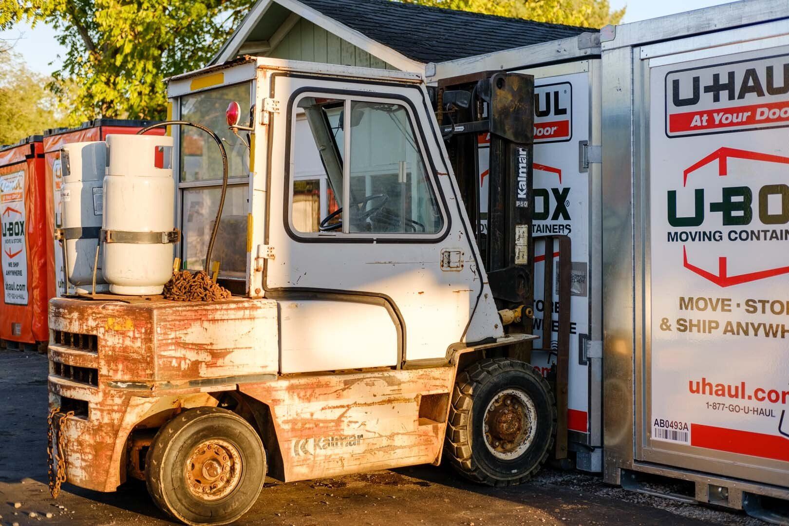 A weathered forklift next to a U-Haul storage container.