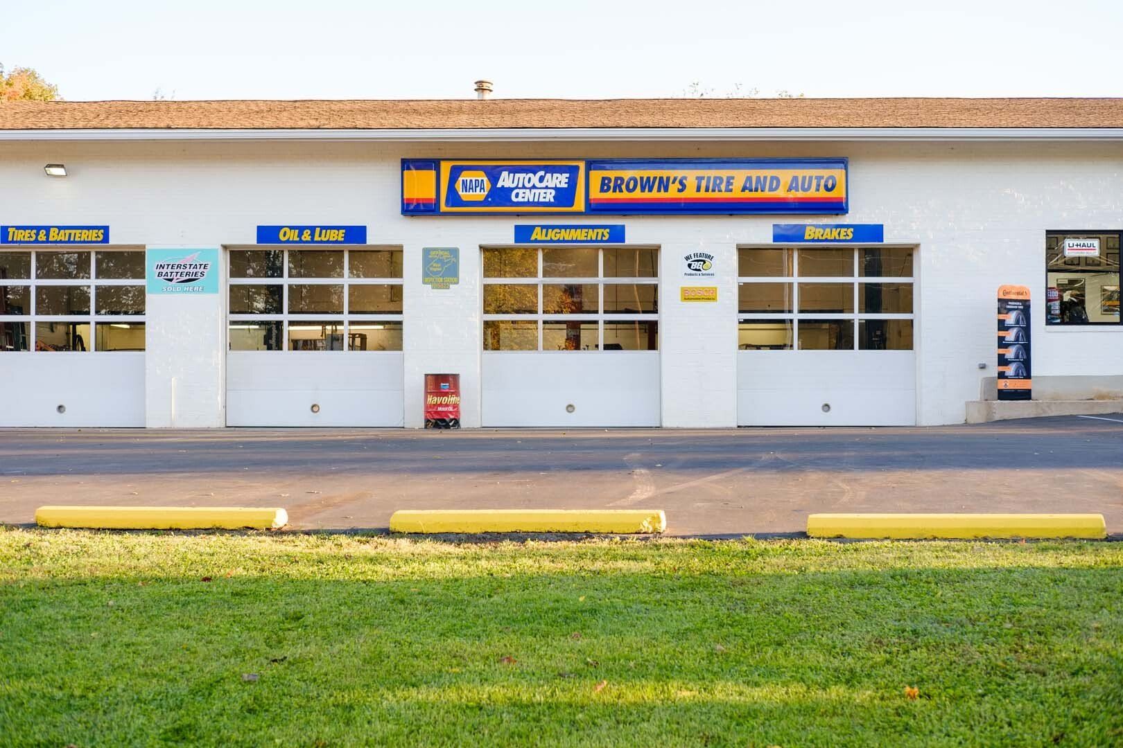 White auto repair shop with garage doors, yellow parking blocks, and a green lawn.