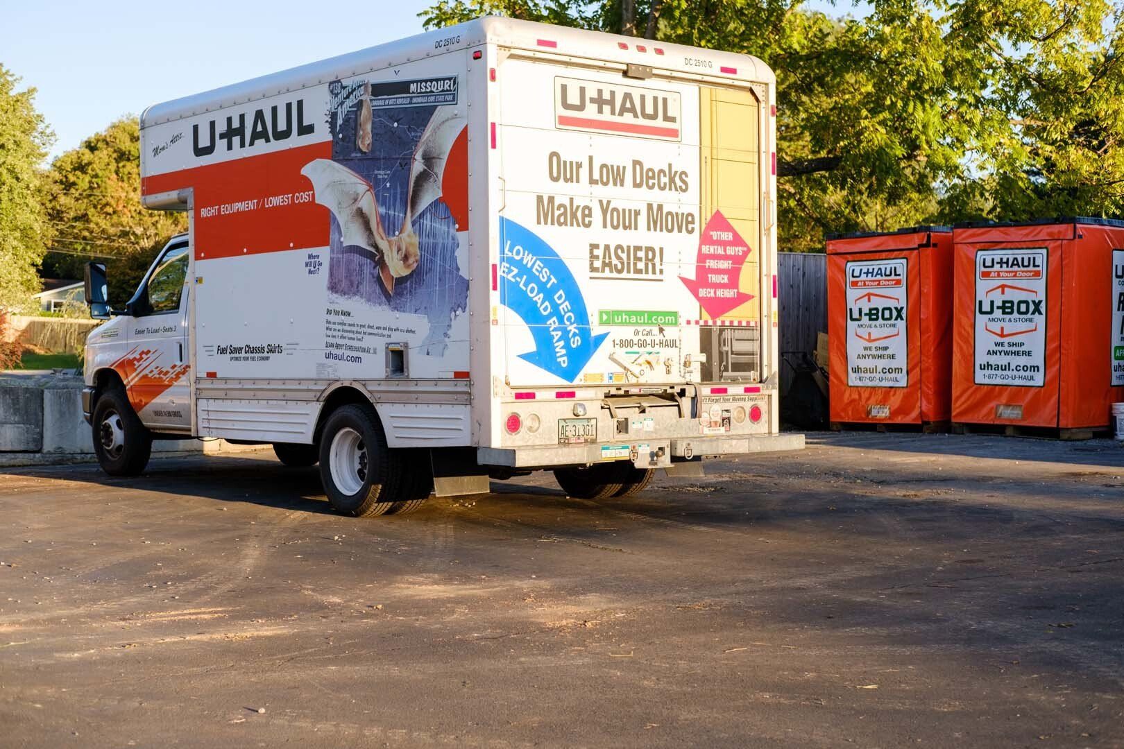 U-Haul moving truck parked on asphalt; two orange U-Box storage containers in the background.