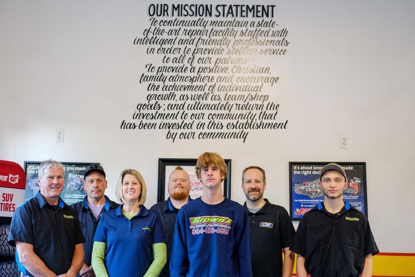 Group of employees standing in front of a mission statement on a wall.