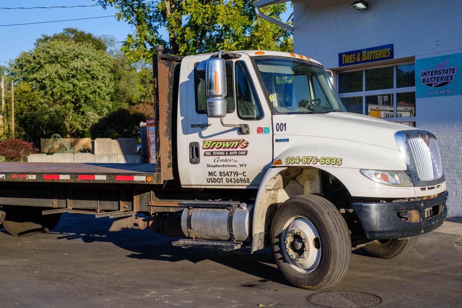 White flatbed truck parked near a building. Truck has company logo and phone number.