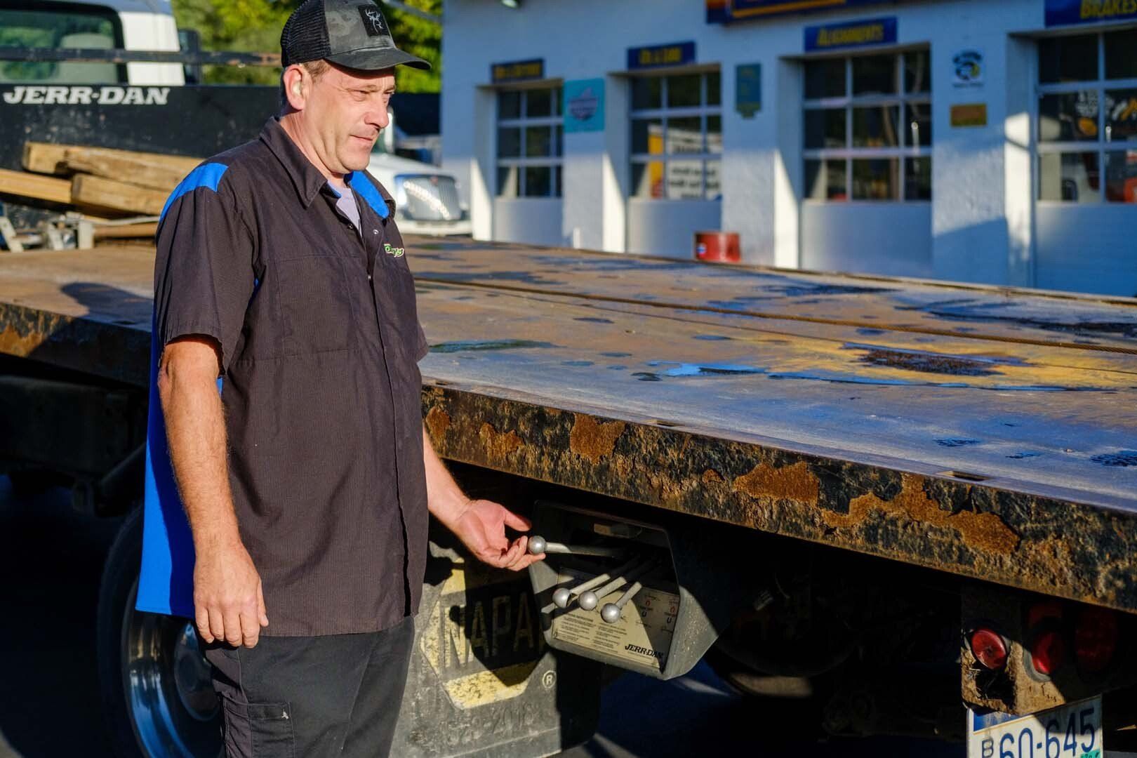Mechanic by a flatbed truck at a shop; he is holding a metal pin.