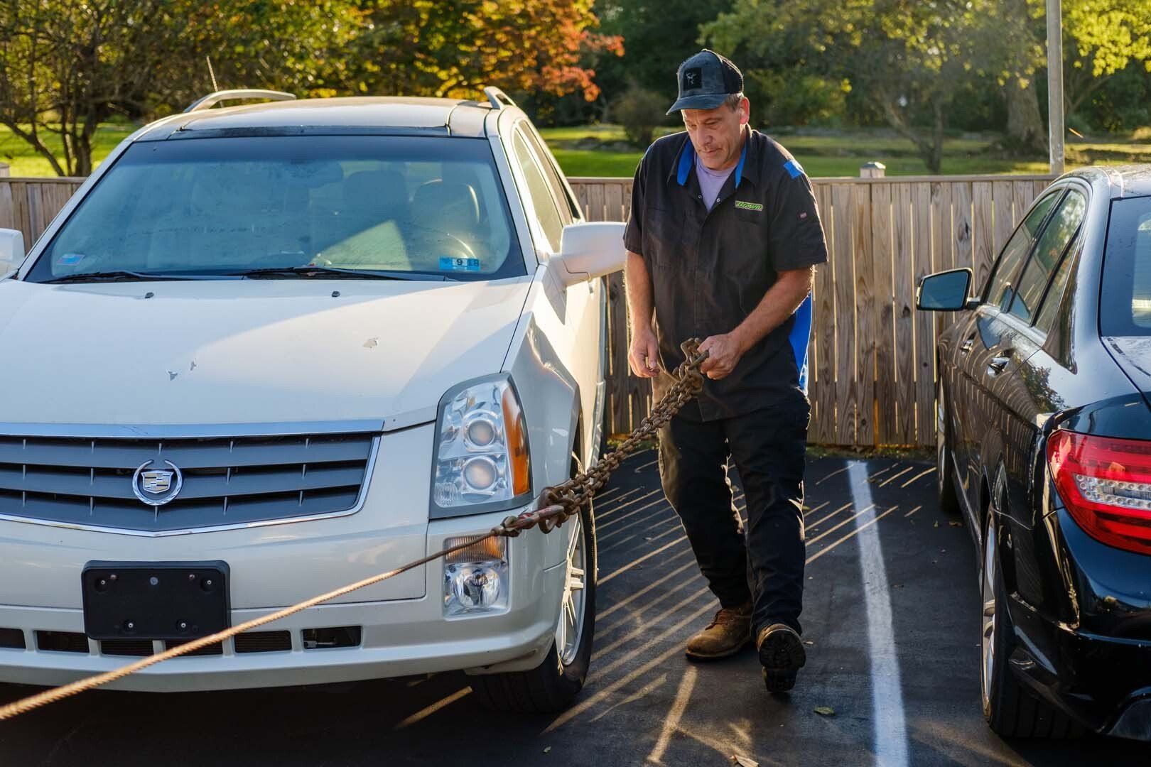Tow truck operator connecting a tow chain to a white SUV in a parking lot.