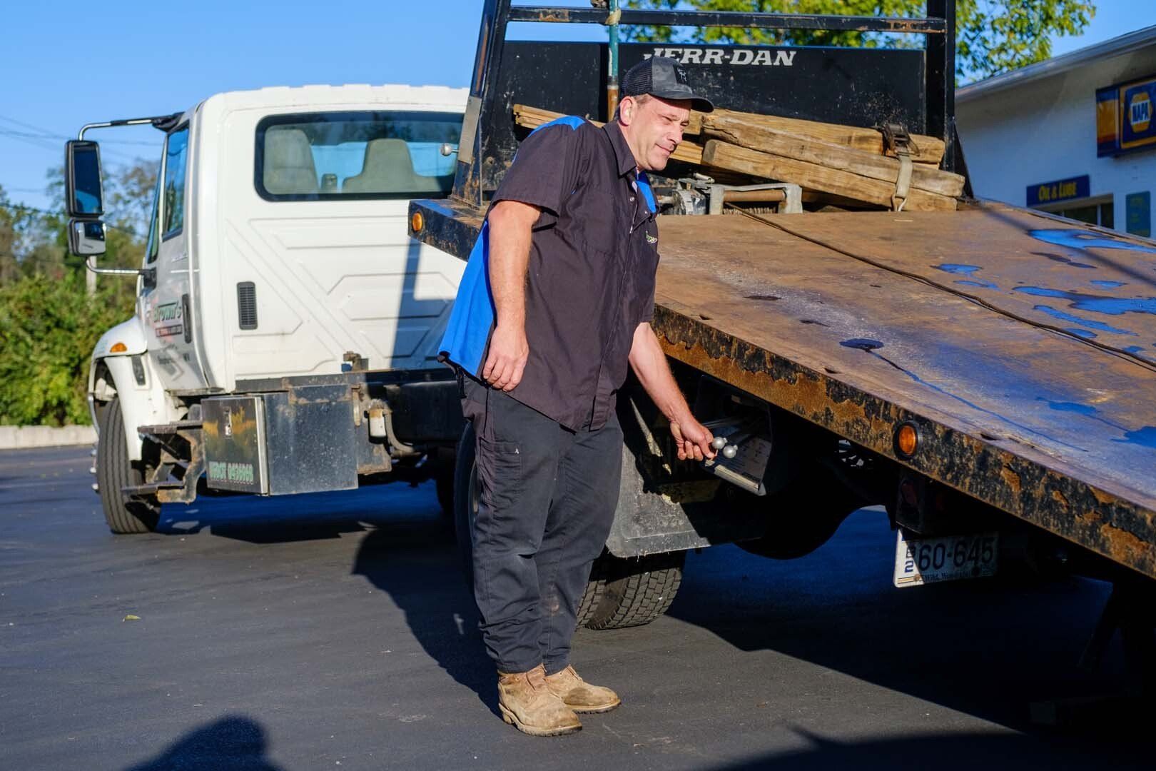 Mechanic in black uniform inspecting a tow truck's flatbed near a building with 