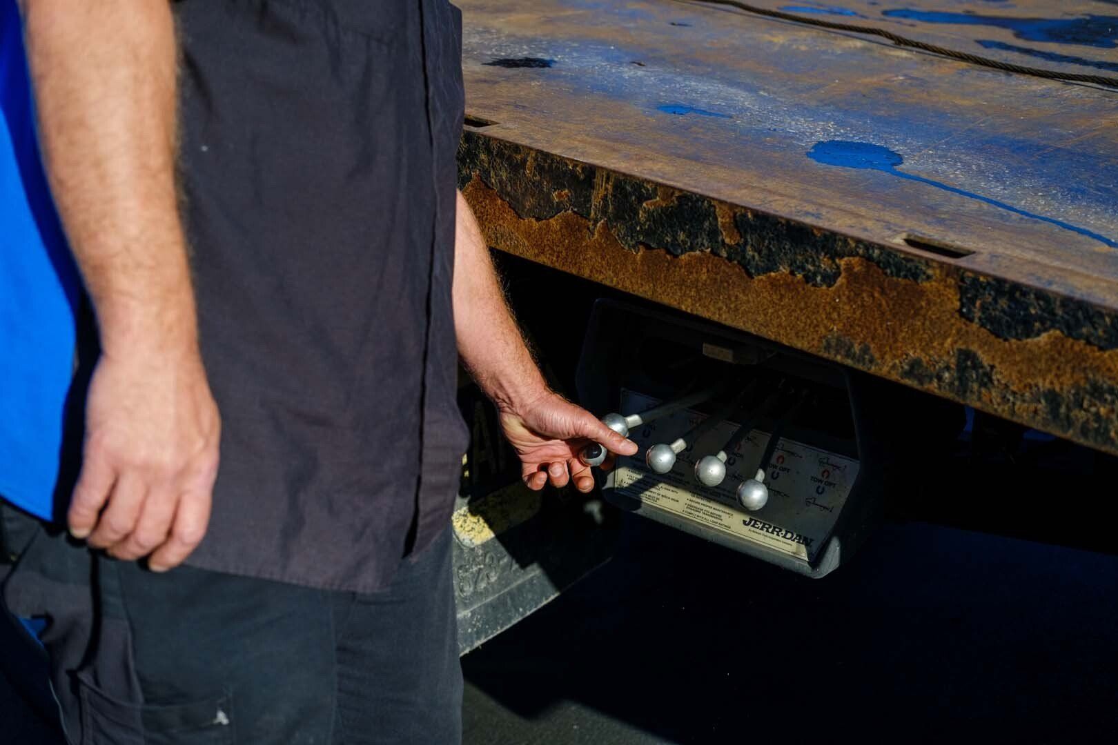 Person in black shirt adjusting silver controls on a trailer's side.