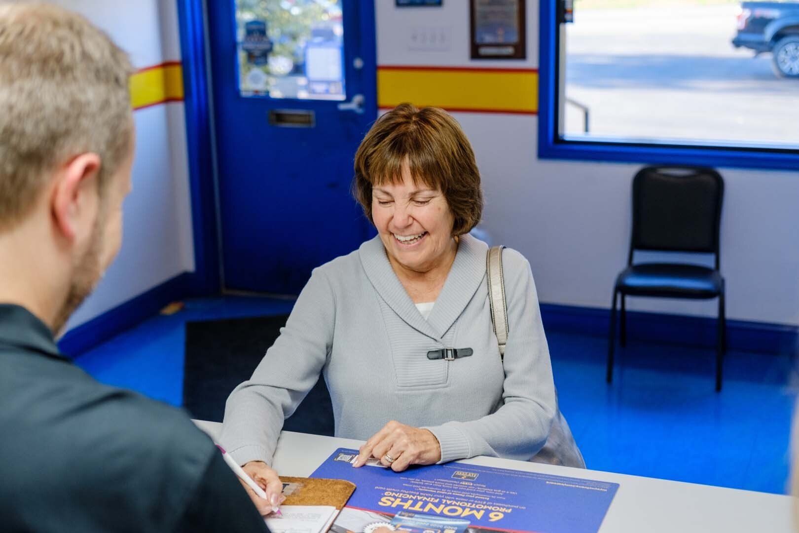 Woman smiling at desk with man in auto shop.