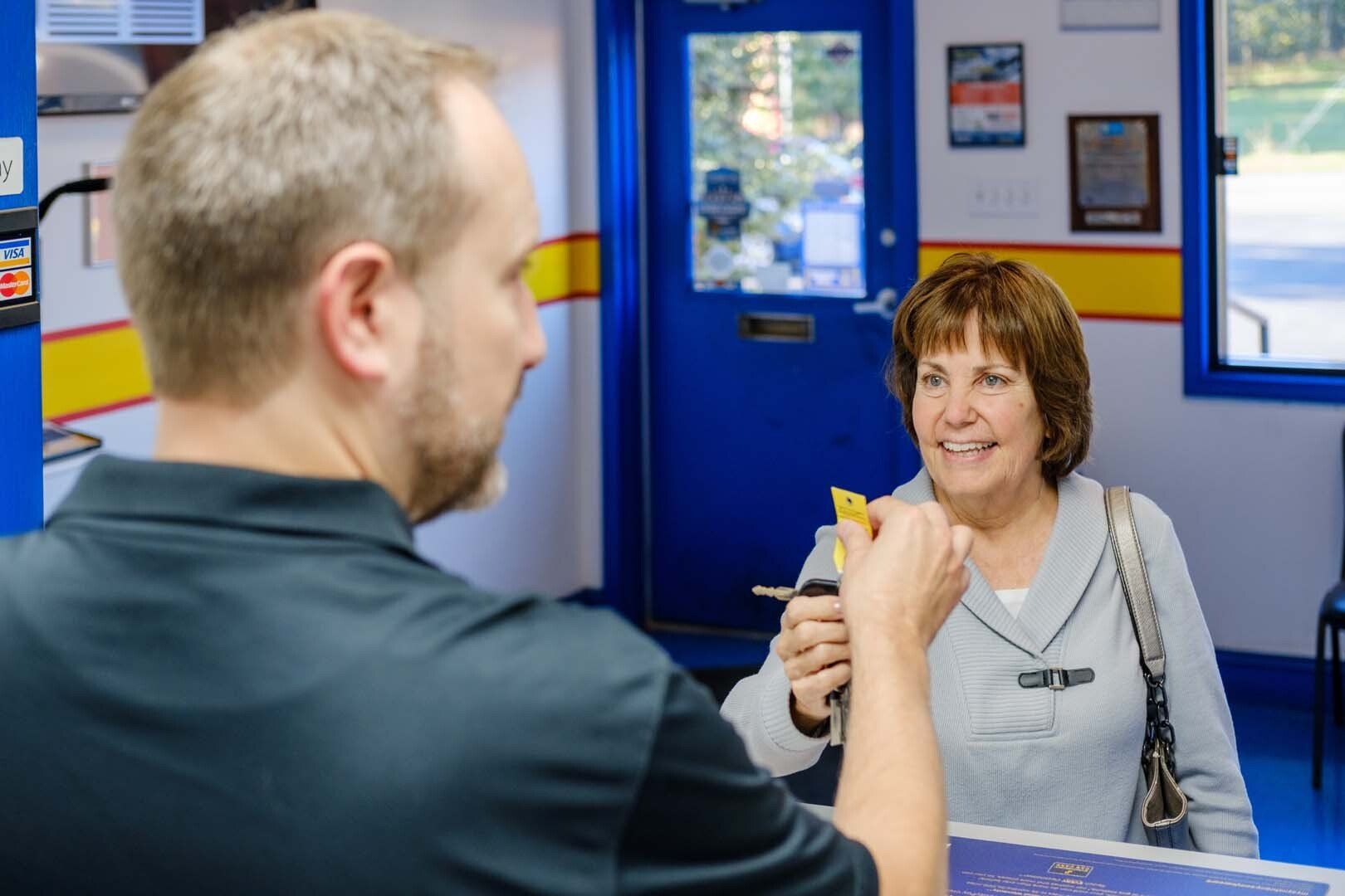 Man hands car keys and card to a woman at a service counter in a shop with blue and yellow accents.