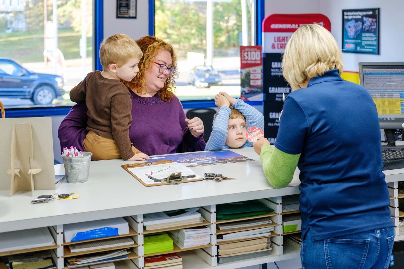 Woman with two children at a counter talking to a person behind the counter in an auto repair shop.