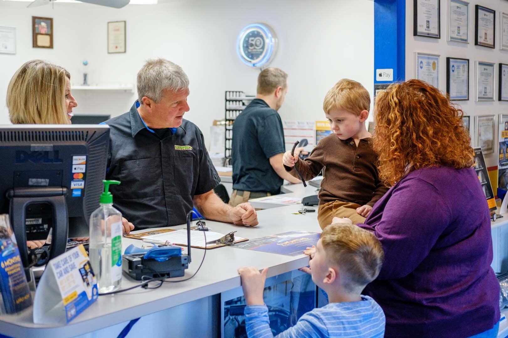 People at the counter of a business, a man talking to a woman holding a child, another boy standing.