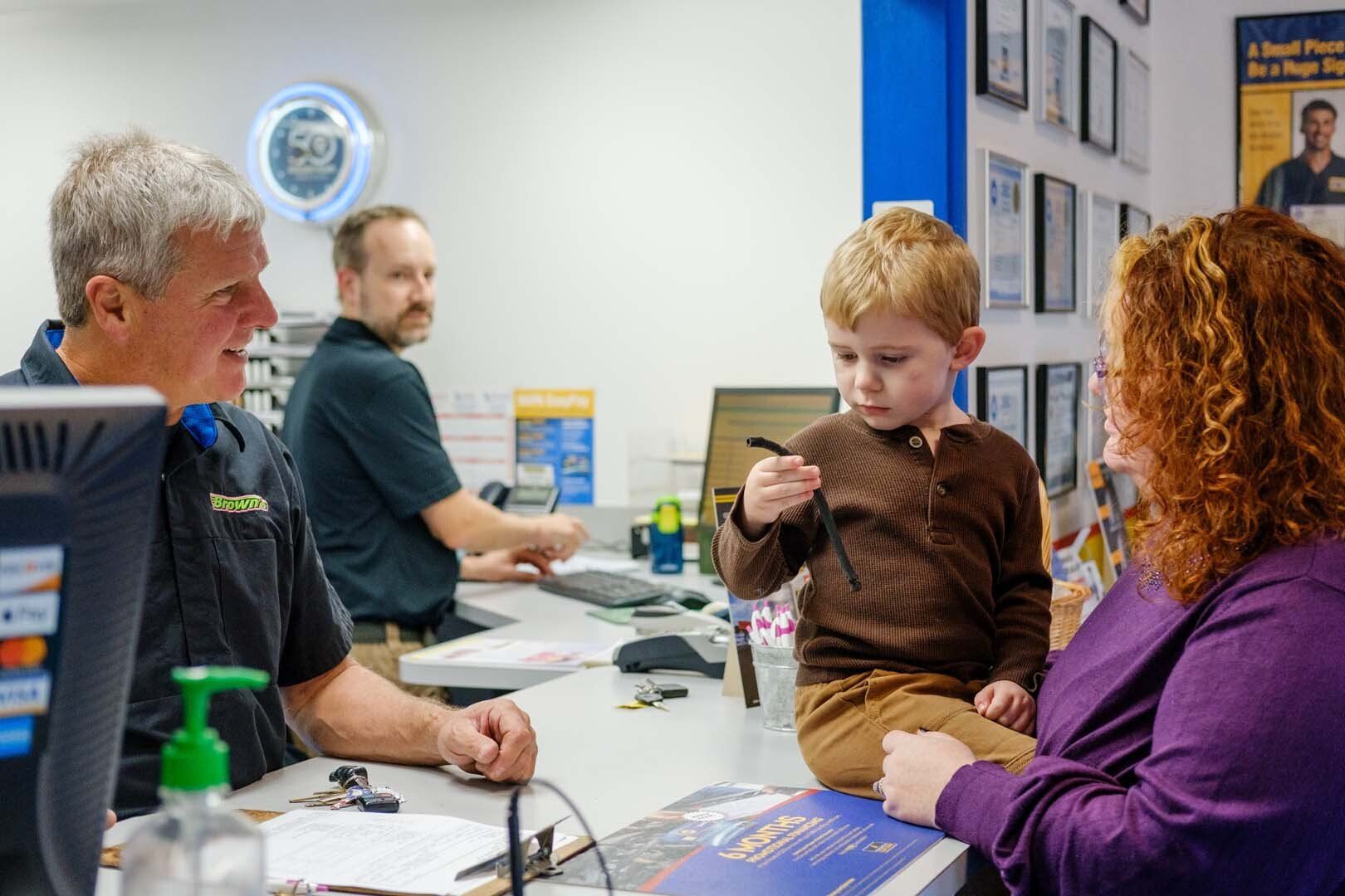 Customer and child at a service counter, talking to a worker. A second employee is in the background.