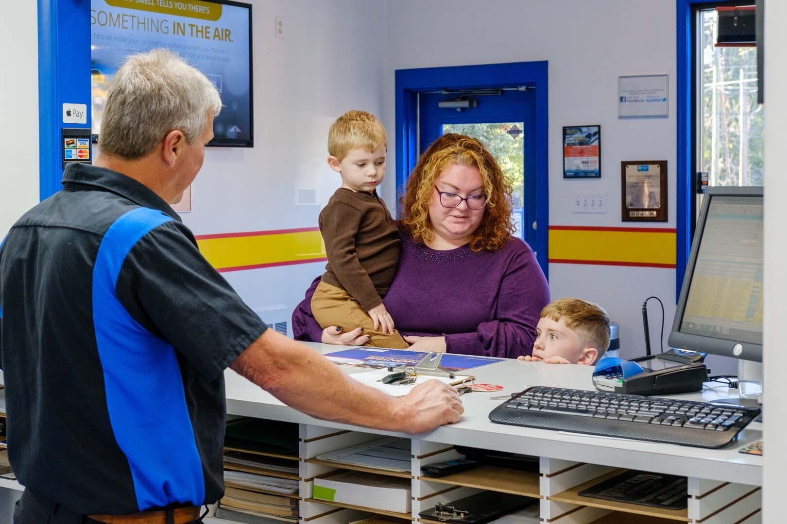 Mechanic talking to a woman and two children at a service counter in an auto repair shop.
