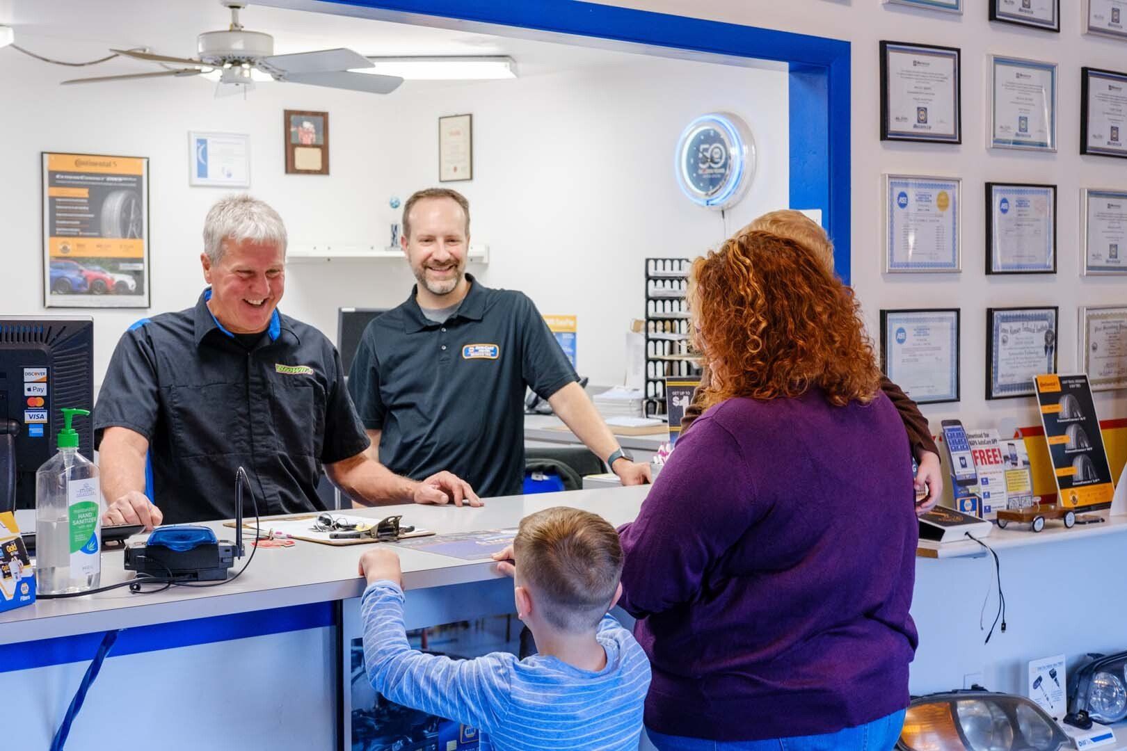Two men at a shop counter assisting a woman and child. White and blue interior. Smiling.