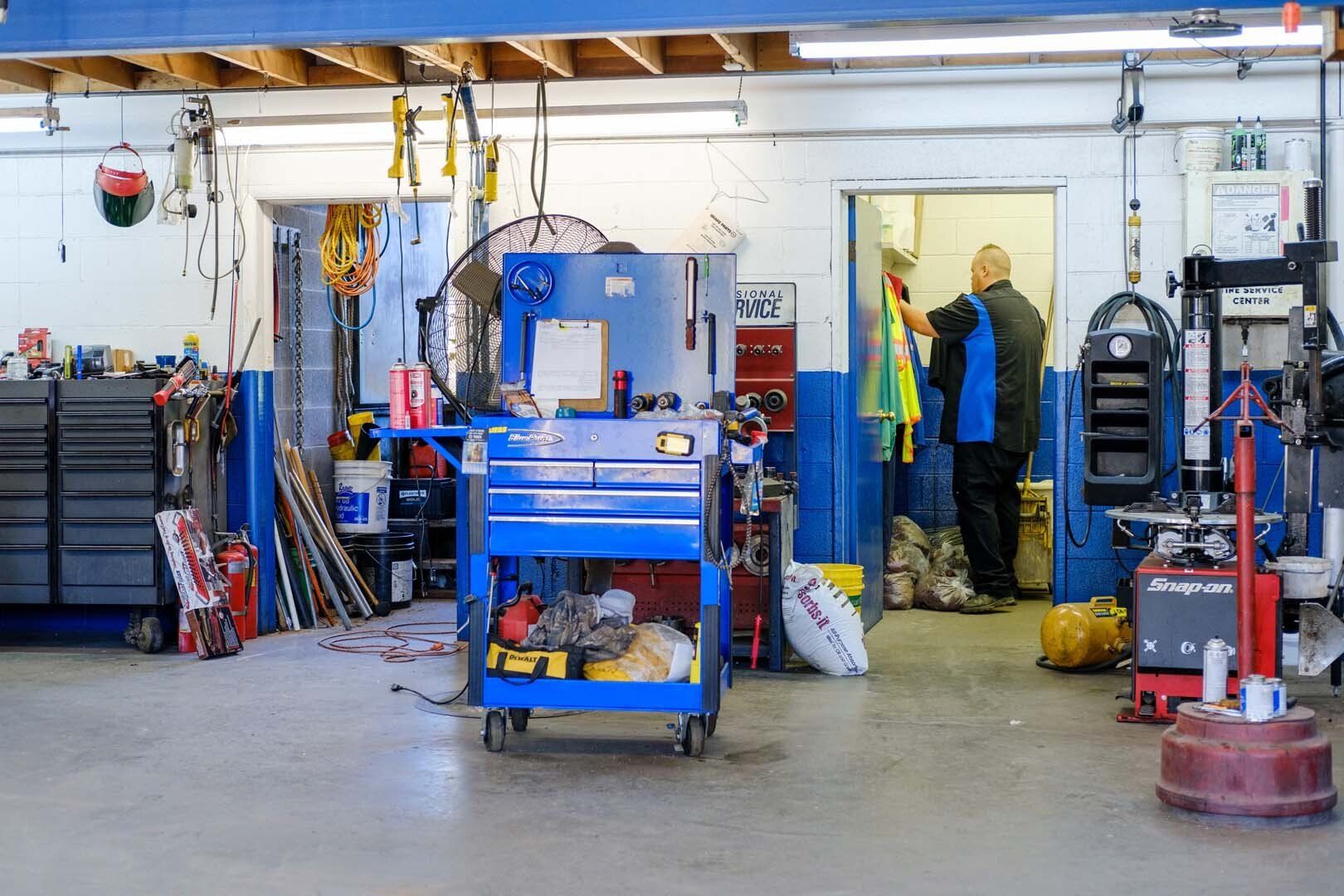 Auto repair shop with tools, blue cart, and mechanic in doorway.
