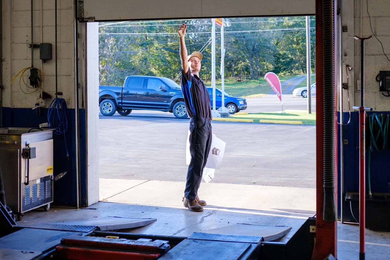 Mechanic raising garage door in auto shop, standing next to a pickup truck.