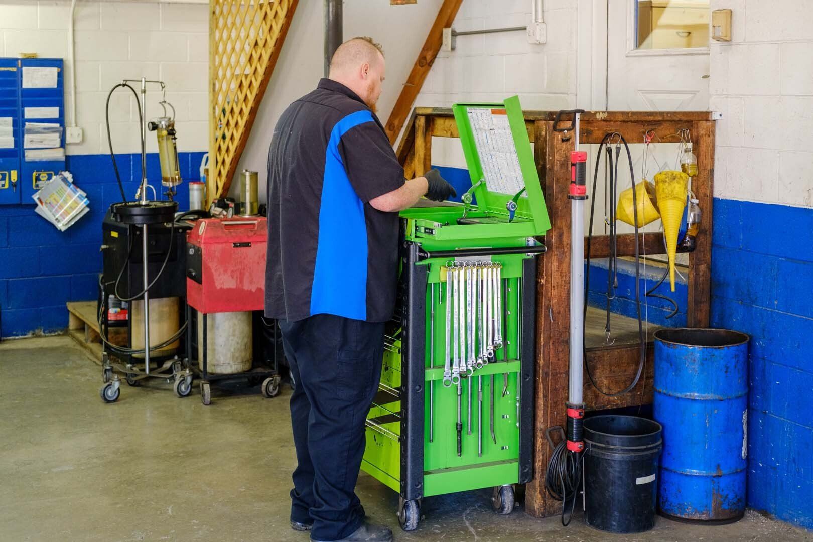 Mechanic in blue and black shirt, using a green tool cart in a garage.
