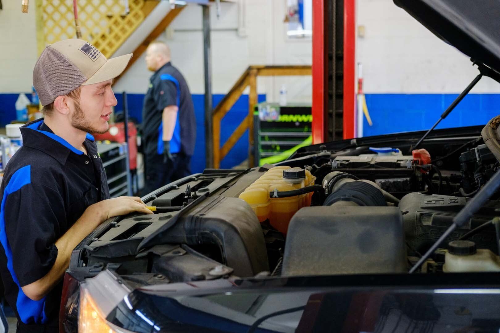 Mechanic in work uniform inspecting a car engine in a repair shop.