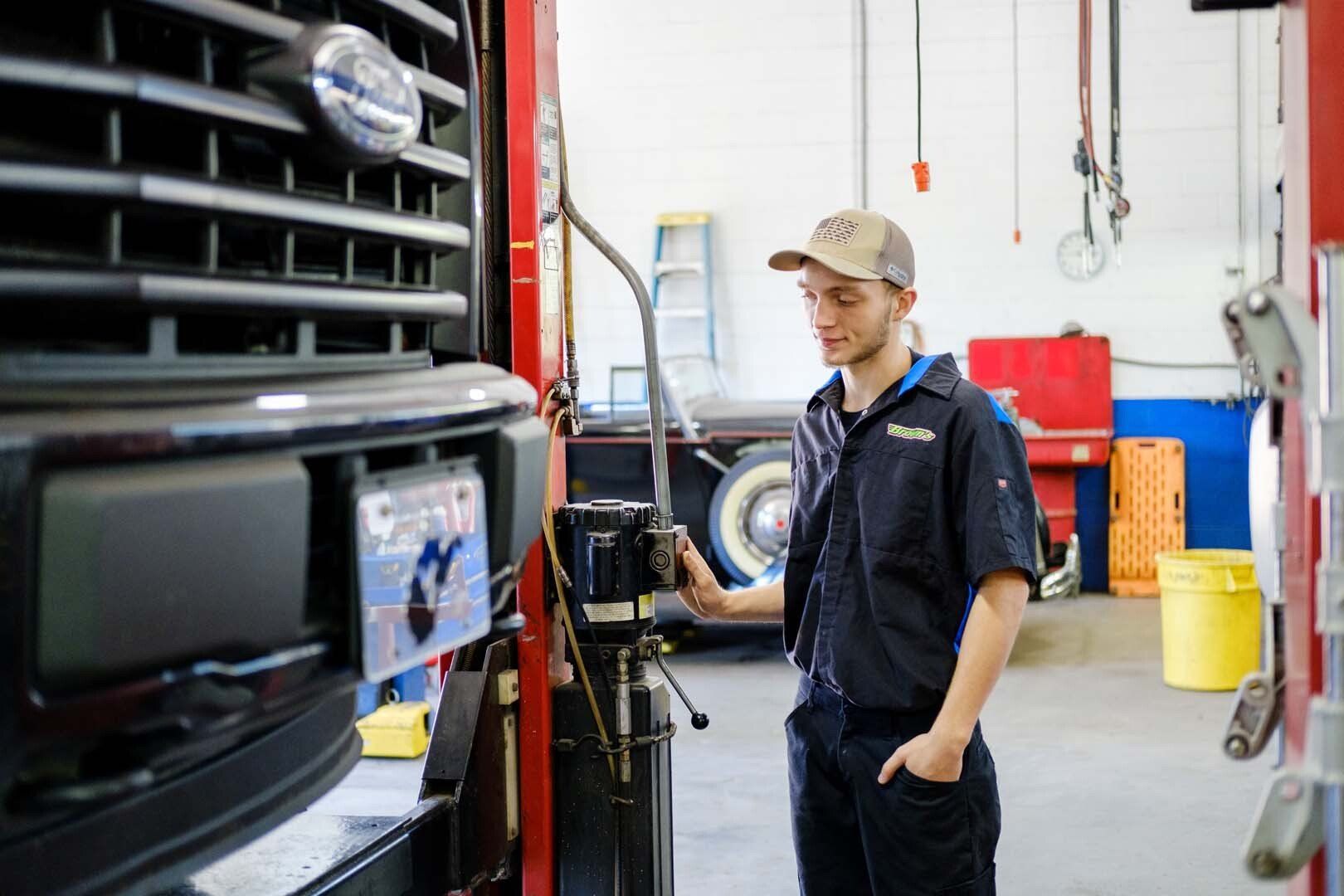 Mechanic inspecting vehicle in a shop. Wearing work uniform and cap, standing next to a truck.