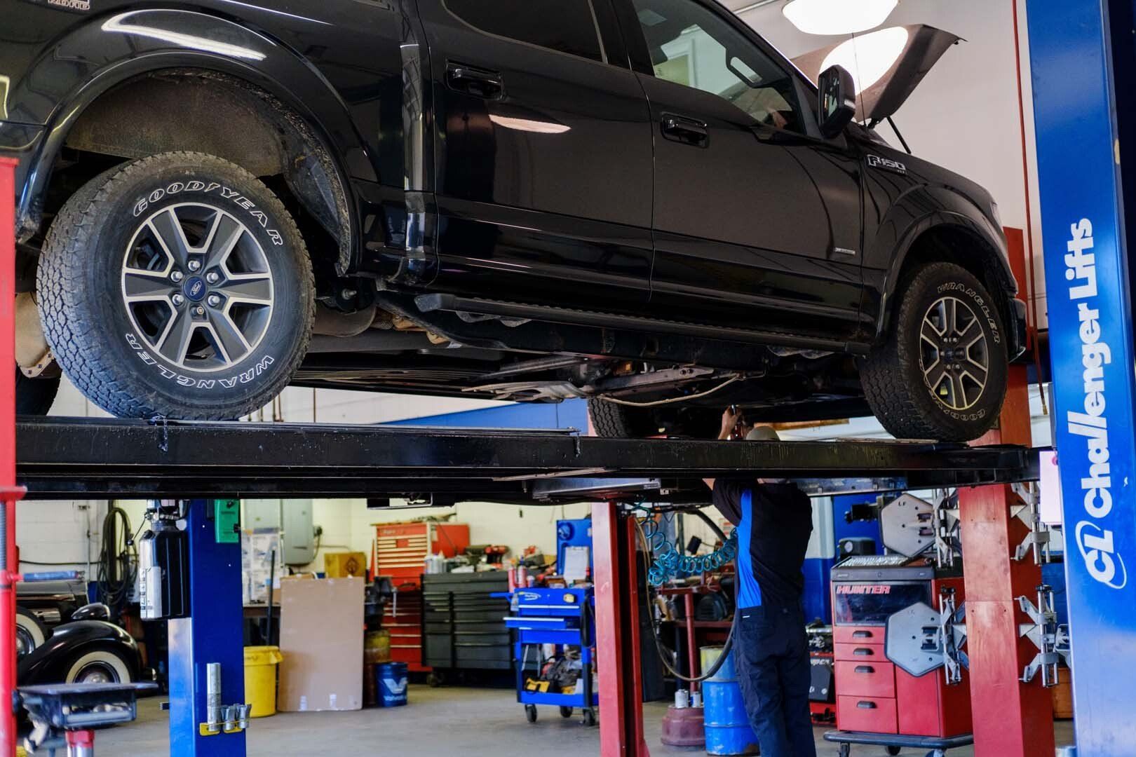 Black pickup truck raised on a car lift in a repair shop.
