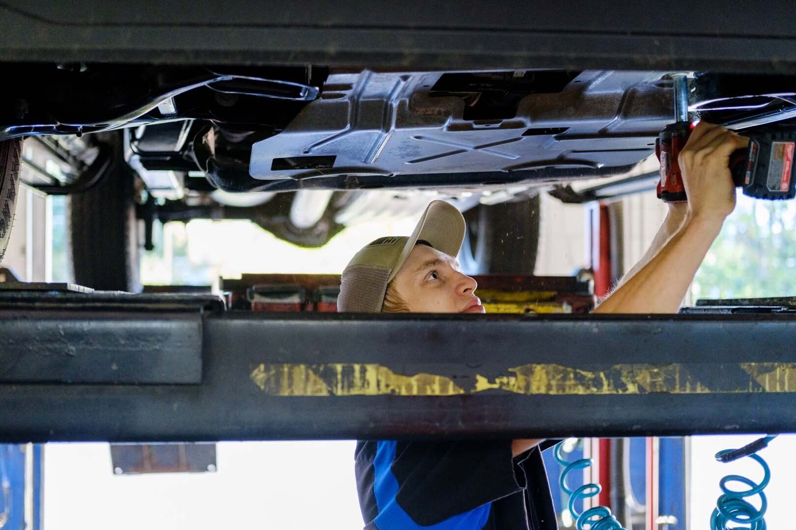 Mechanic working under a car, using a power tool in a garage.