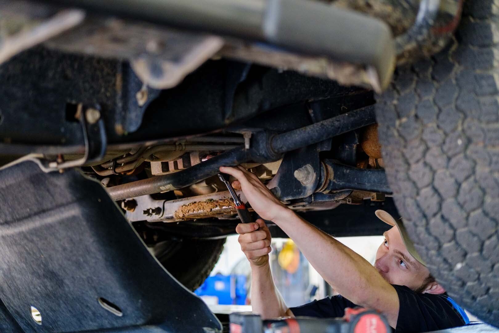 Mechanic working on a car from below, using a wrench. Underneath the vehicle with tires visible.