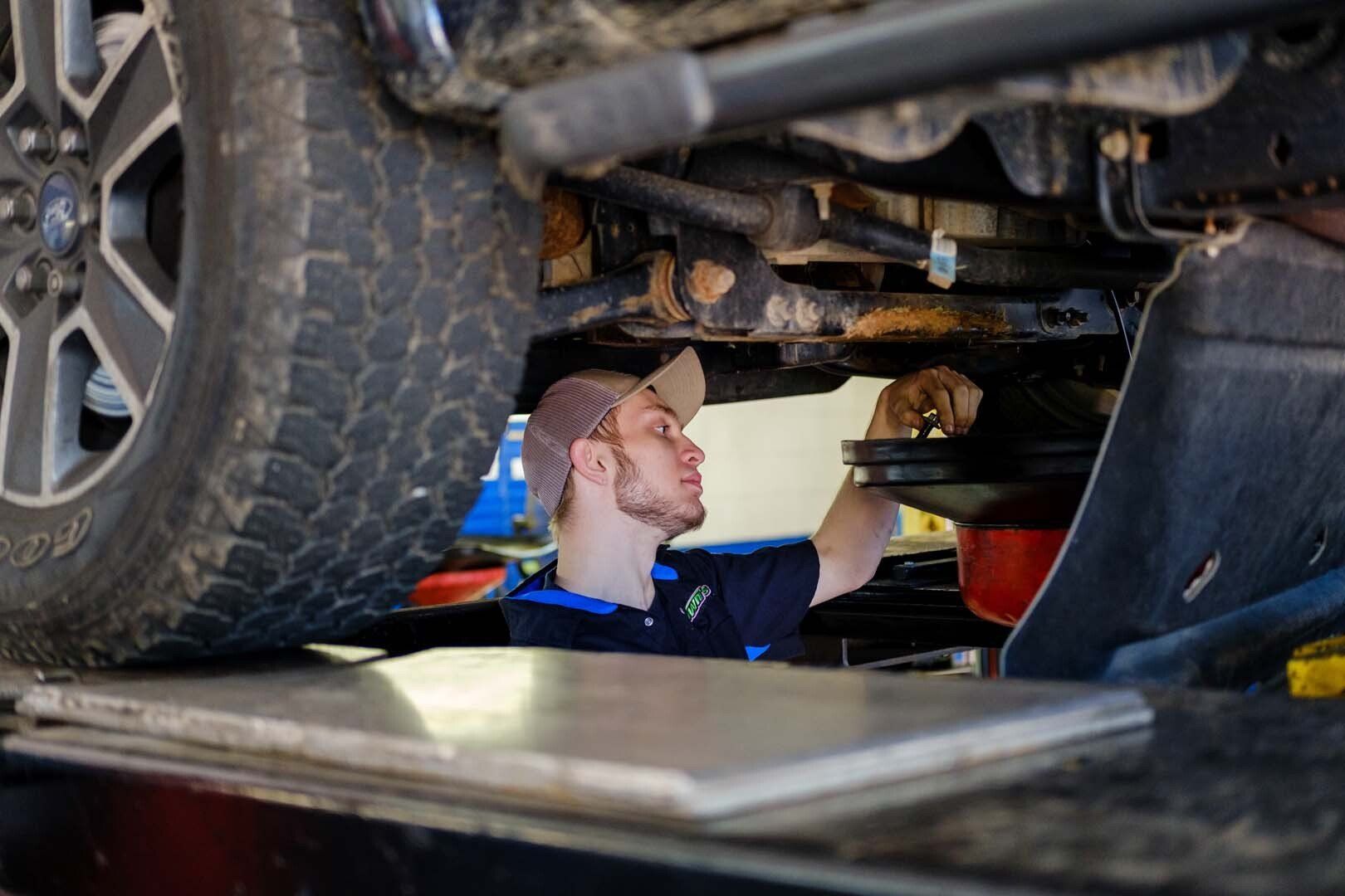 Mechanic under a vehicle changing oil in a shop.