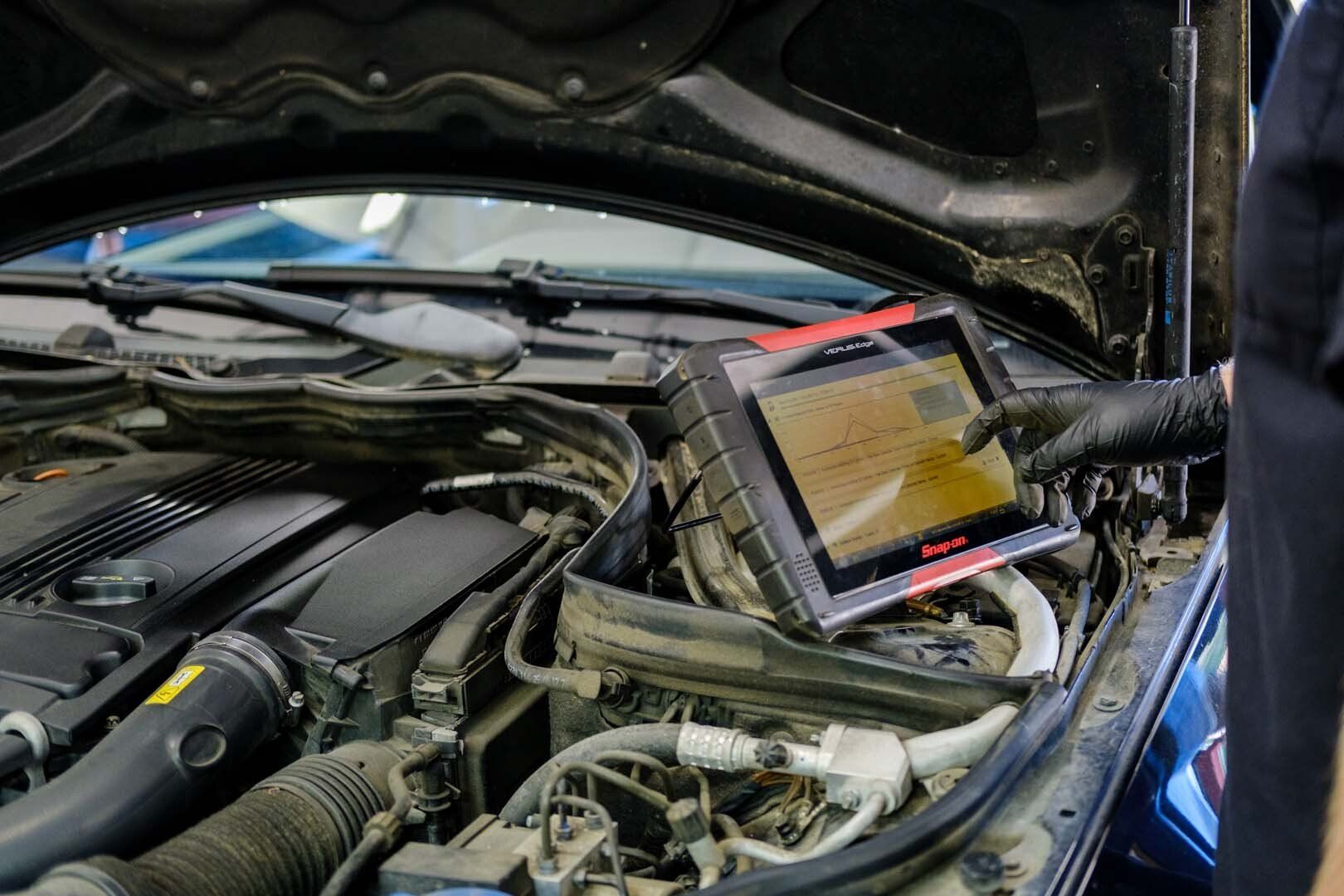 Mechanic using diagnostic computer on a car engine, in a garage setting.