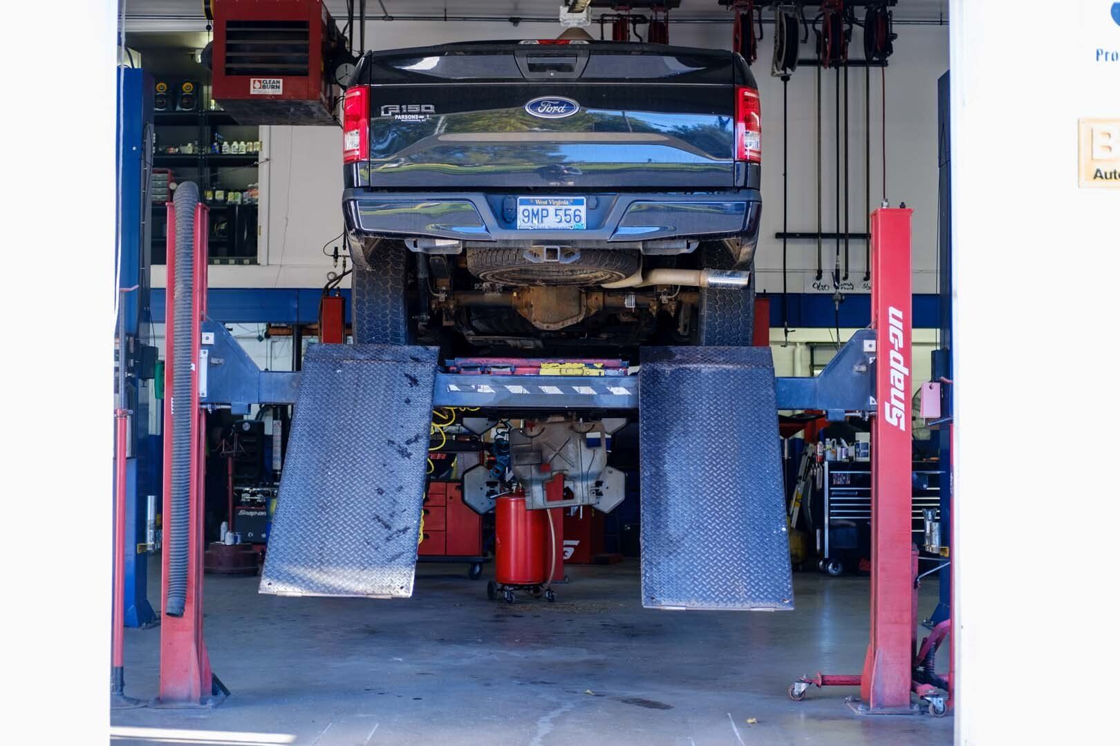 Truck on a Snap-on lift in a garage, rear view. Black truck, red lift, mechanic shop setting.