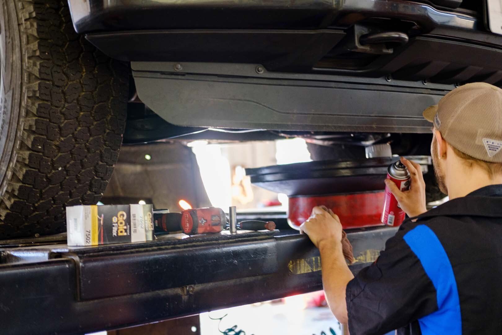 Mechanic changing oil on a vehicle raised on a lift; oil drain pan visible.