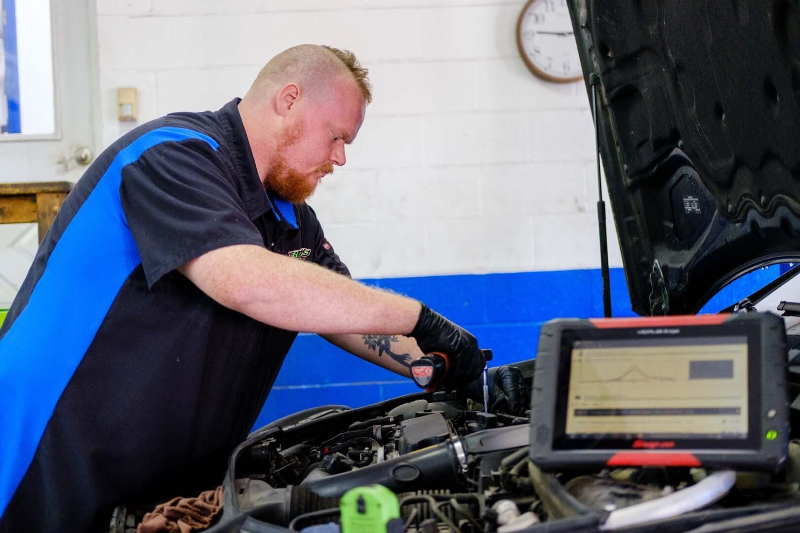Mechanic working on car engine, using diagnostic tablet in a garage.