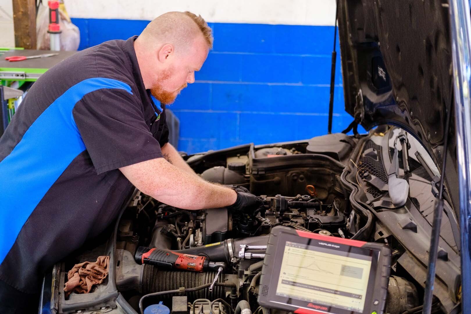 Mechanic working on car engine, using diagnostic tool. Blue and black work shirt.