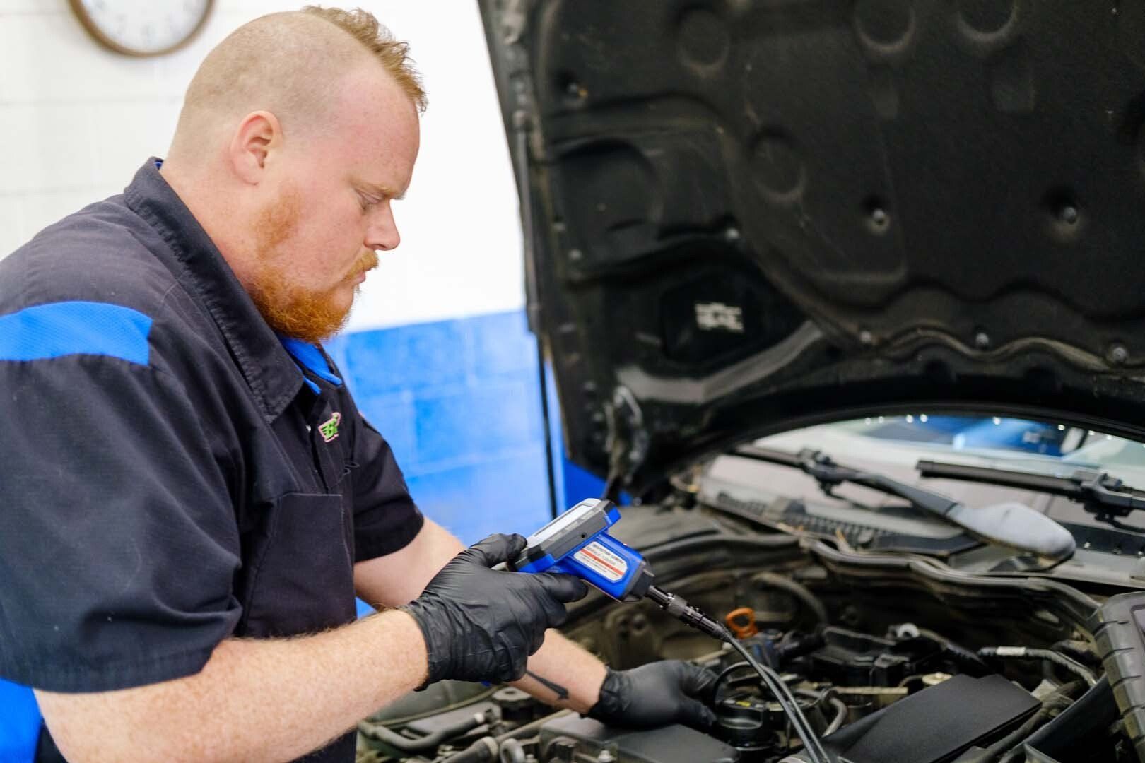 Mechanic working on a car engine with a tool, wearing gloves and a blue-accented shirt.