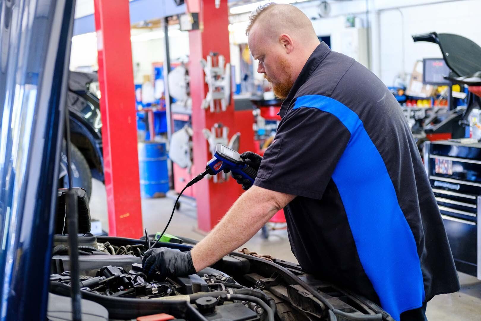 Mechanic in blue and black uniform working on a car engine in an auto repair shop.