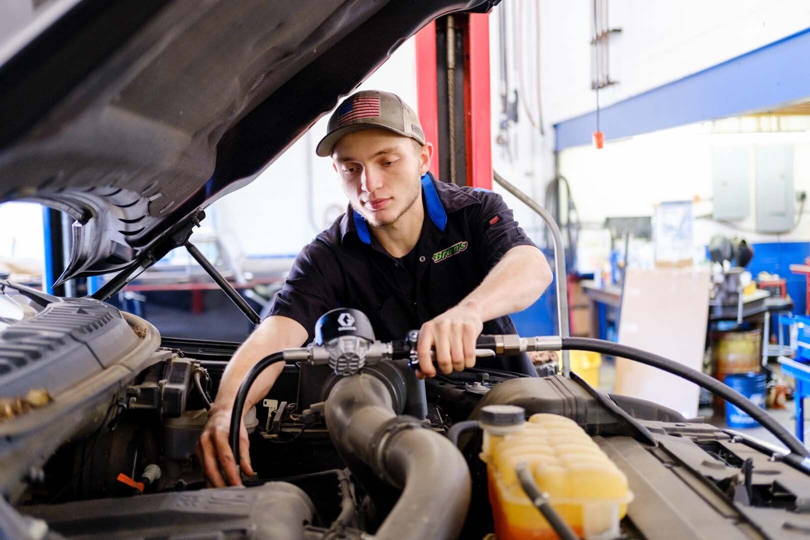 Mechanic working on car engine in a garage. Wearing a cap and holding a tool, focused.