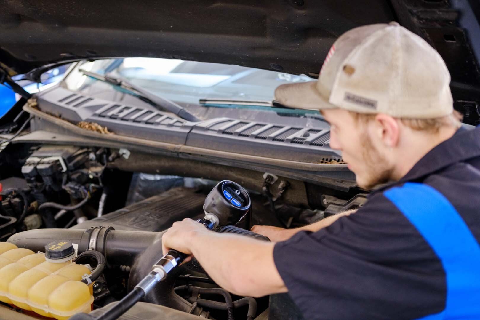Mechanic working on a truck engine with a gauge; under the hood, smiling.