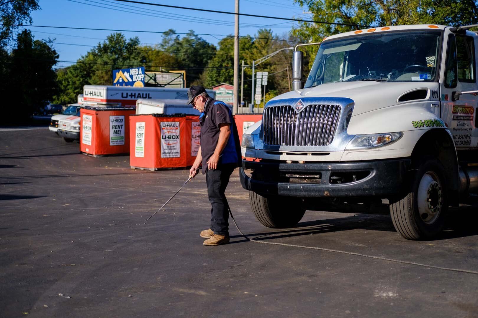 Man inspects a white truck with U-Haul boxes in a parking lot on a sunny day.