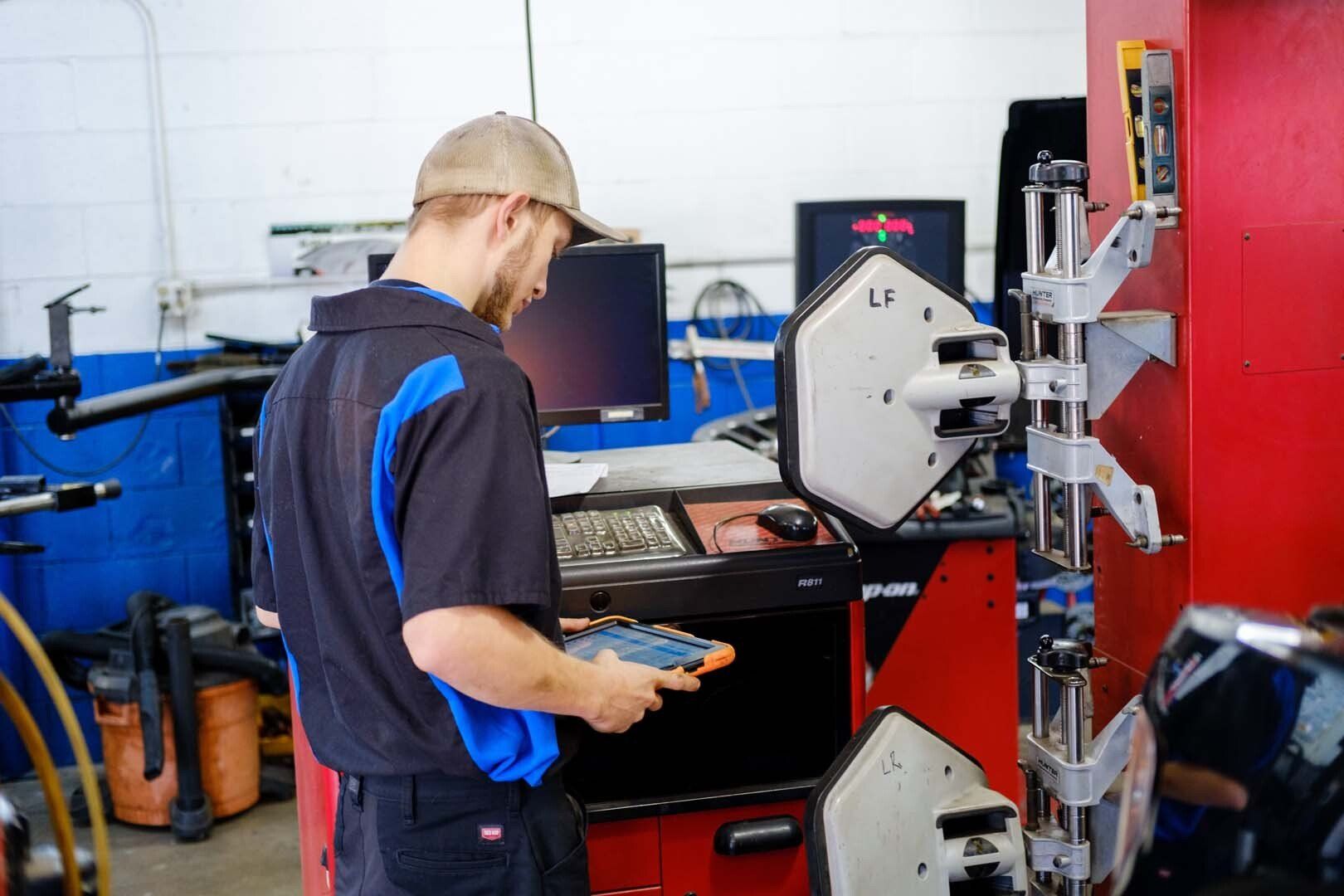 Mechanic using alignment machine in a shop. He holds a device, looking at the computer screen.